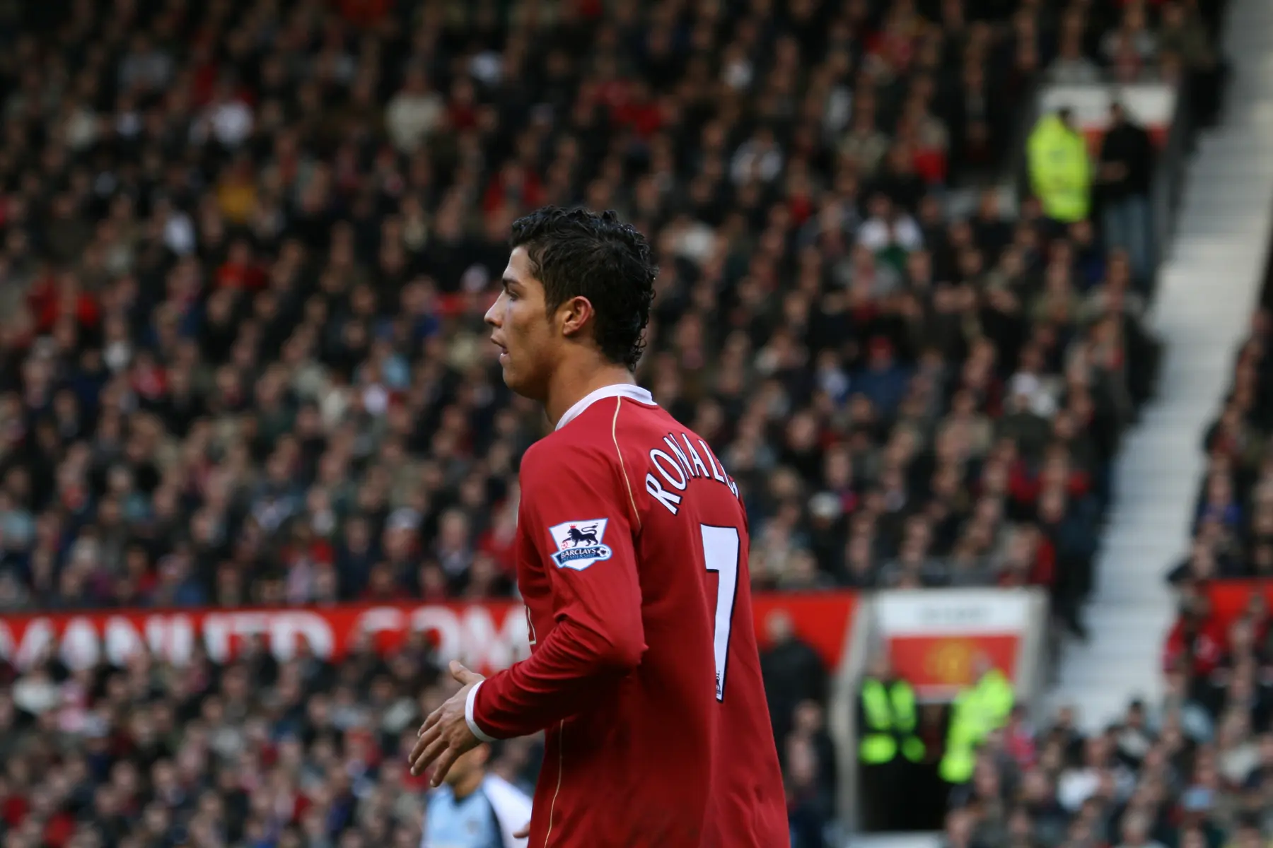 Cristiano Ronaldo de perfil, vestindo a camisa vermelha do Manchester United em um estádio lotado.